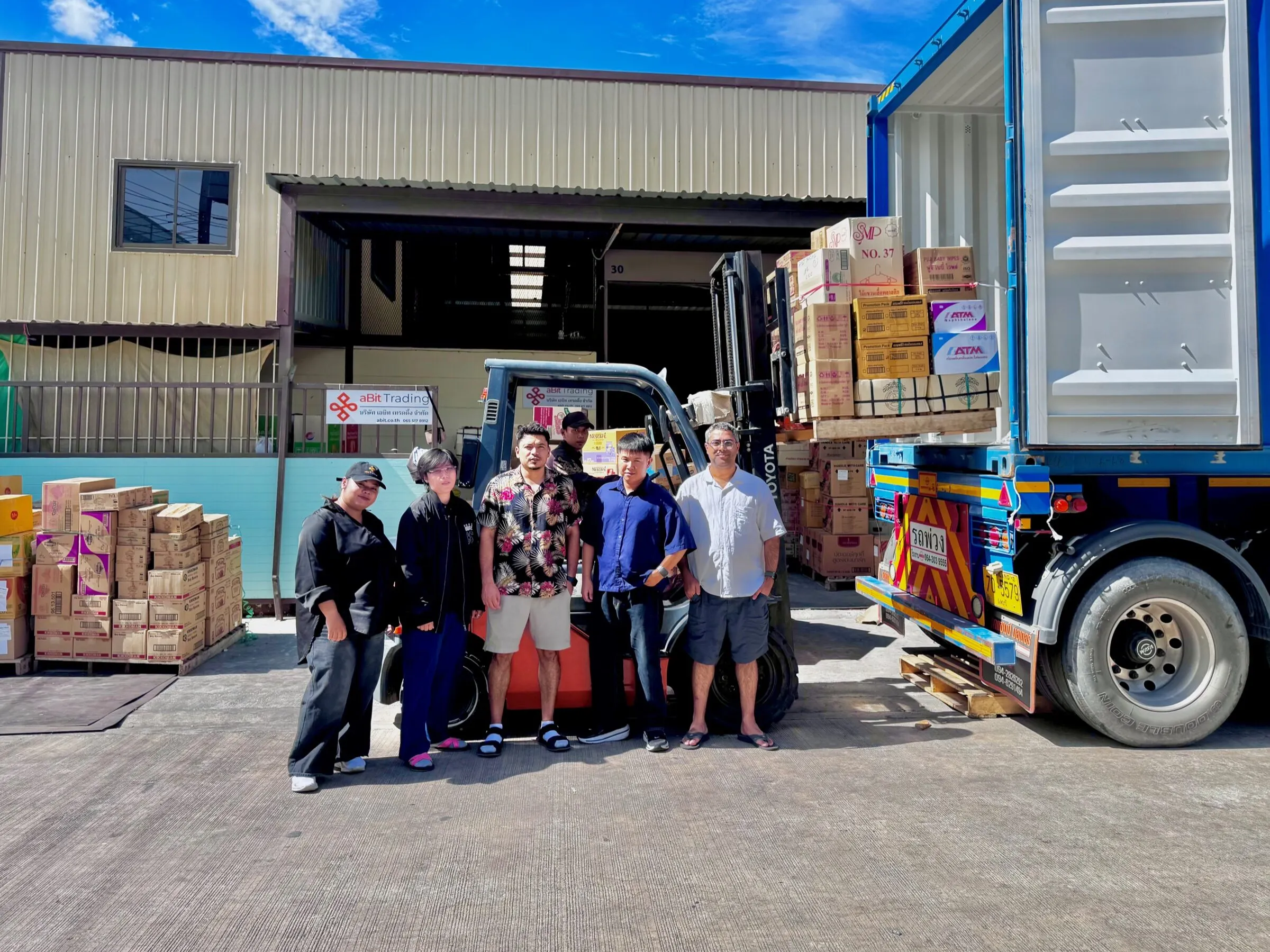 aBit Trading team members beside a forklift and a container being loaded with palletised cartons at the Bangkok warehouse