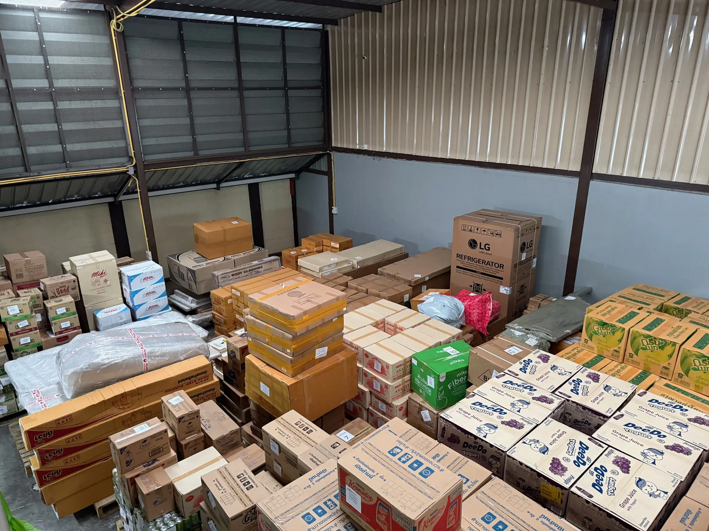 Cartons of mixed consumer goods — juice, creamer and household items — stacked inside the warehouse ahead of consolidation