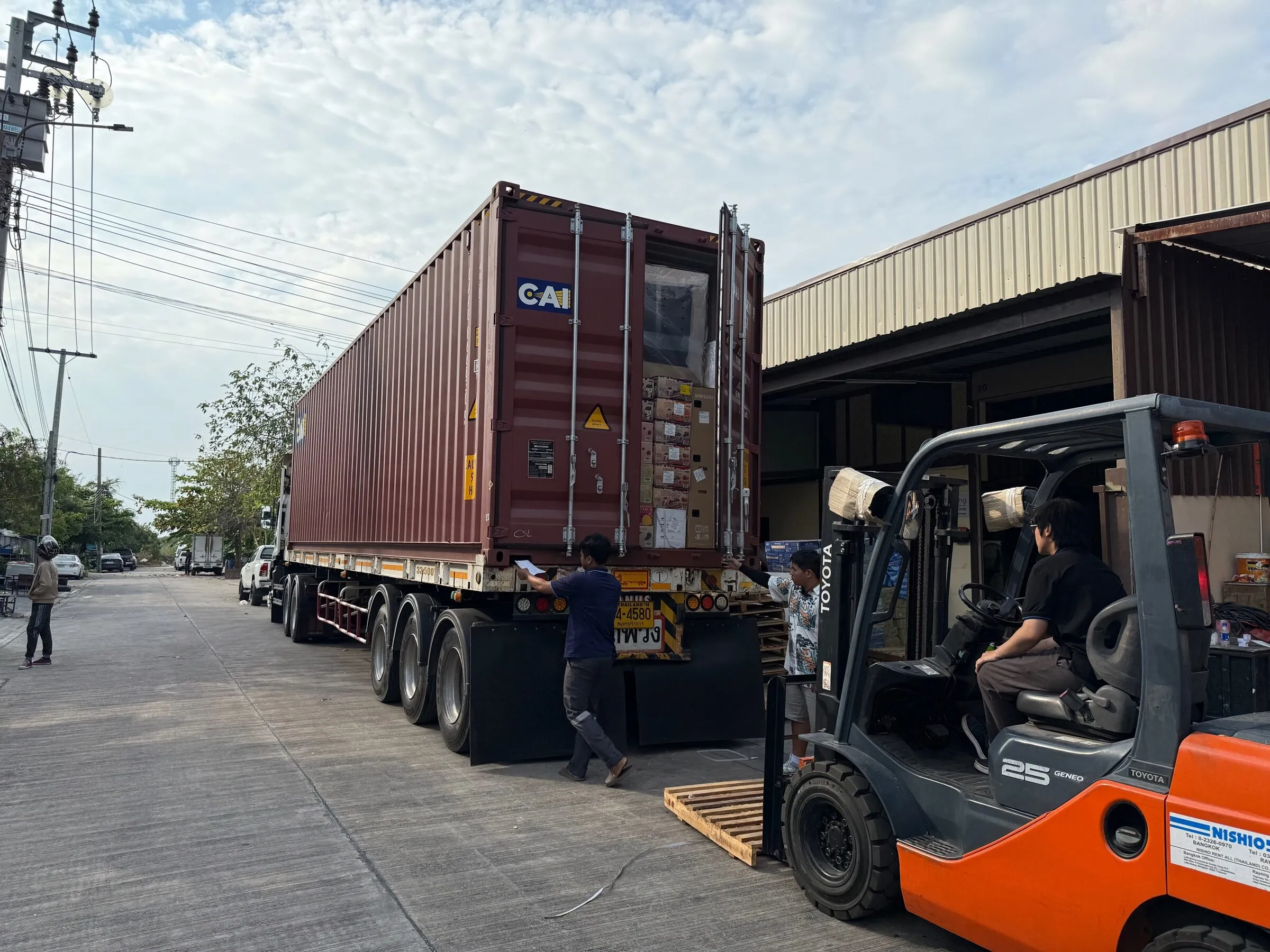 A staff member checking the loading list at the open doors of a packed container outside the warehouse